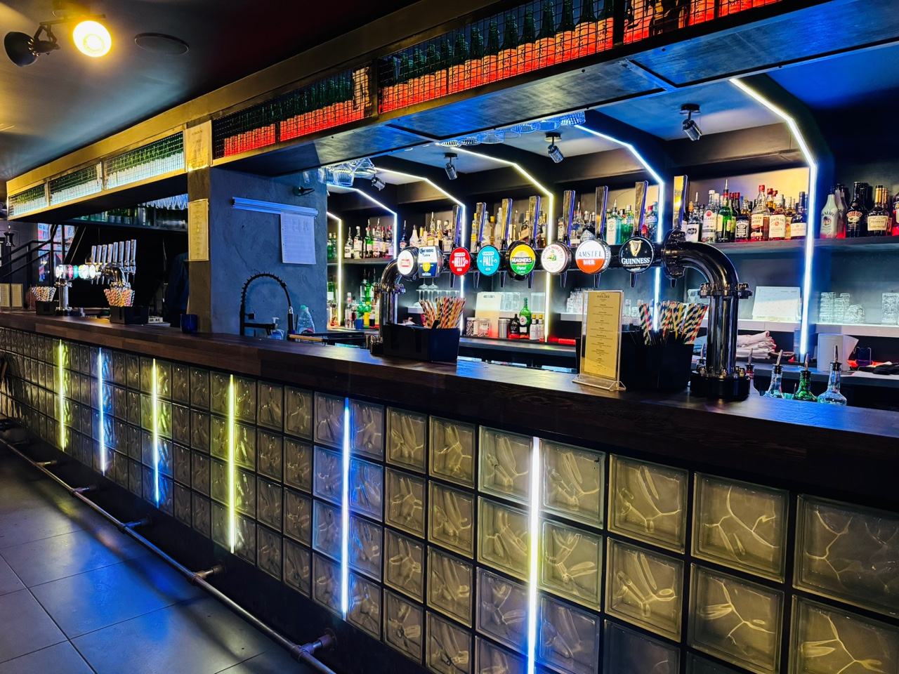 The HANJAN bar counter, taps and back bar lit by blue neon above a glass-brick front