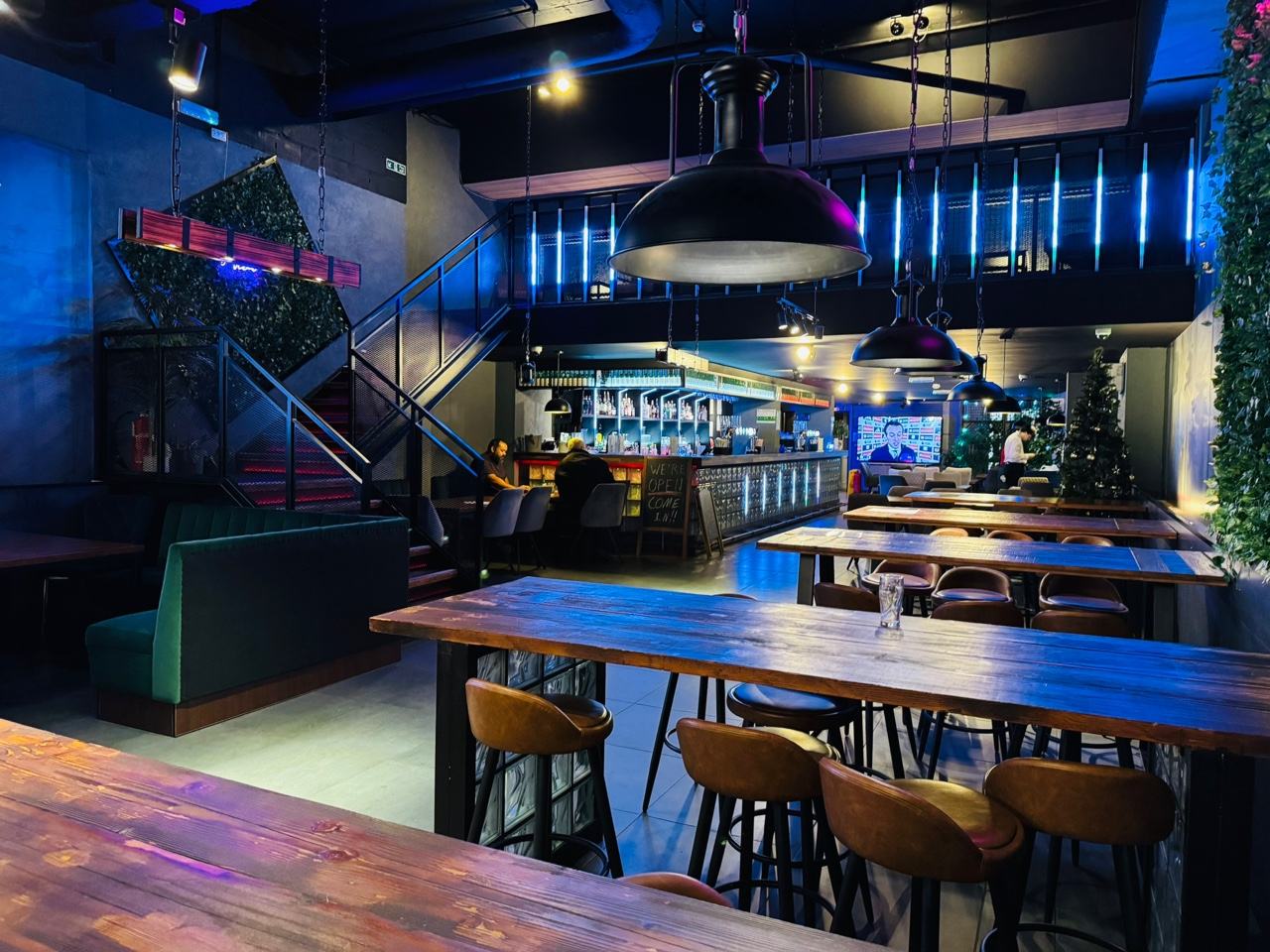 The main floor at HANJAN: long wooden communal tables and stools, the bar and screens behind, blue neon along the ceiling