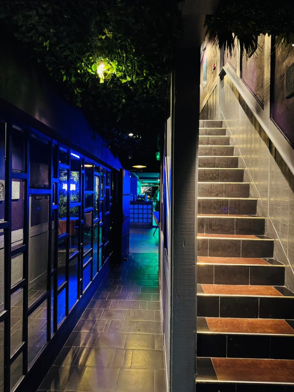 The entrance to HANJAN: a lit stairwell beside the blue neon of the bar windows